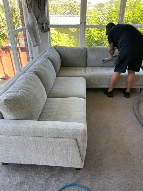Technician cleaning a large fabric corner sofa